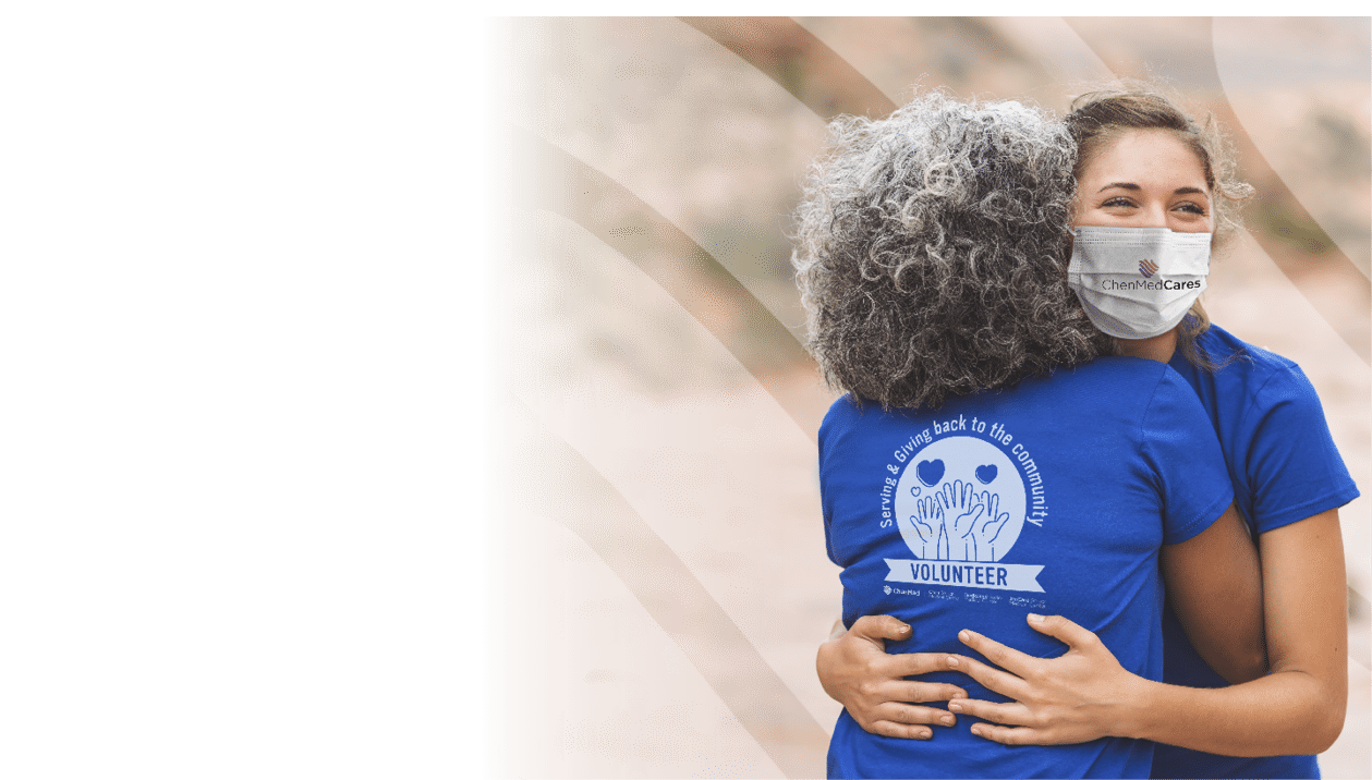 Two volunteers give each a hug before the big event - a race in the desert  The shot is over the shoulder of a senior ethnic woman and is focused on a smiling Caucasian millennial-age woman 